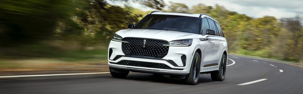 White luxury SUV driving on a curving road with motion blur, surrounded by greenery.