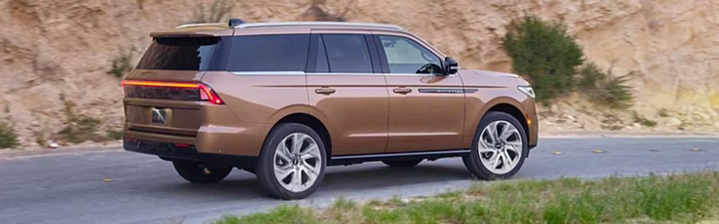 Side view of a brown luxury SUV driving on a paved road alongside a rocky hillside.
