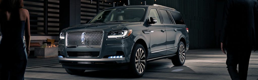 Gray Lincoln Navigator luxury SUV parked outside a modern upscale building at night.