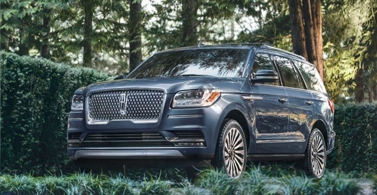 Blue Lincoln Navigator SUV parked among lush trees, highlighting its signature grille and elegant full-size exterior.