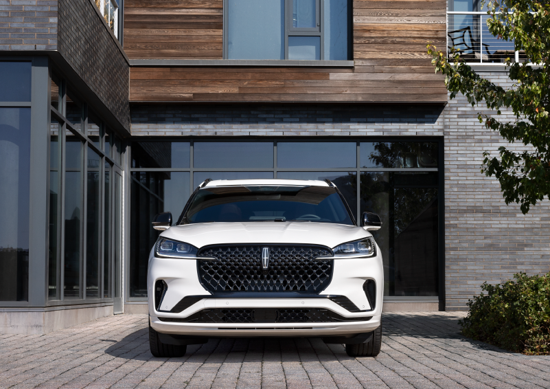 A white 2025 Lincoln Aviator® SUV is shown parked outside a modern building with gray brick and wood accents. | West Point Lincoln of Sugar Land in Houston TX