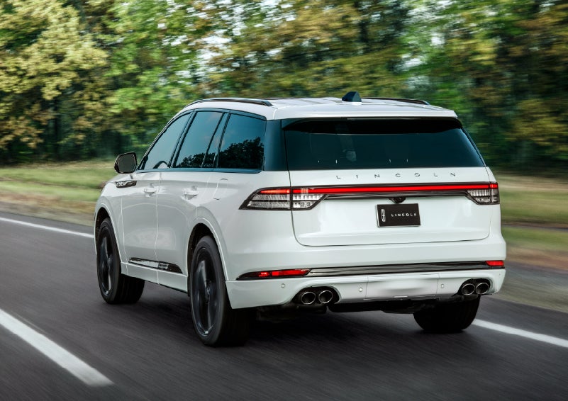 A white 2026 Lincoln Aviator® SUV is being driven away down a road lined with colorful trees. | West Point Lincoln of Sugar Land in Houston TX