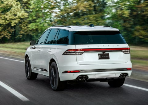A white 2026 Lincoln Aviator® SUV is being driven away down a road lined with colorful trees. | West Point Lincoln of Sugar Land in Houston TX